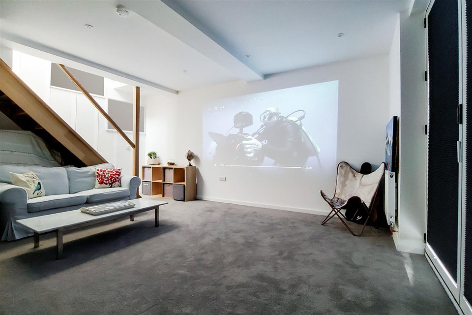 A newly built garden building showing a basement seating area with a projector projecting onto the large white rear wall.