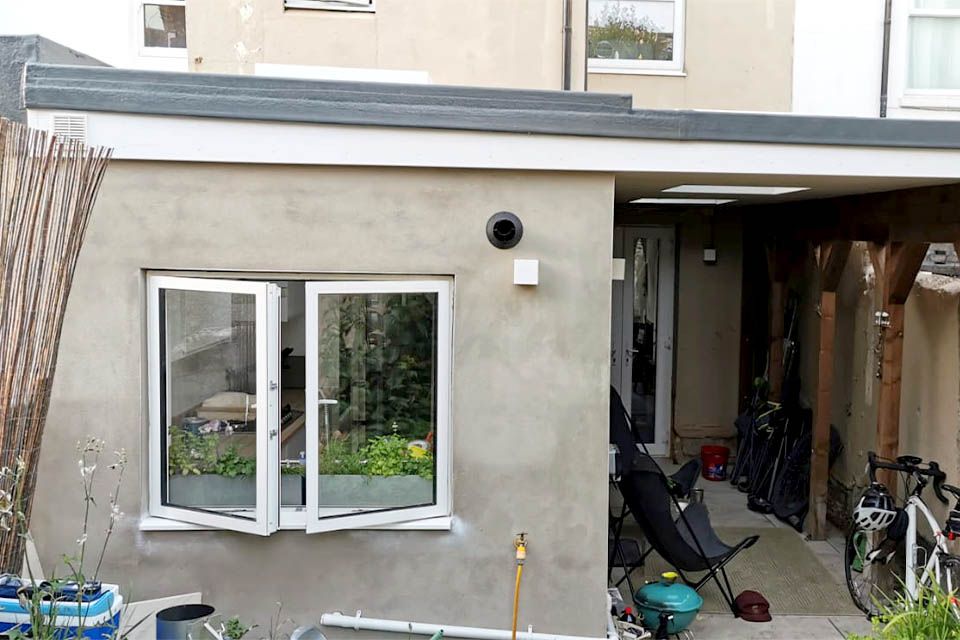 A newly built, unrendered rear extension with canopy at the rear of a terraced house.