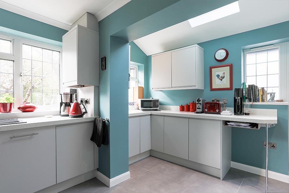 An extended kitchen with white cupboards and nordic blue walls.