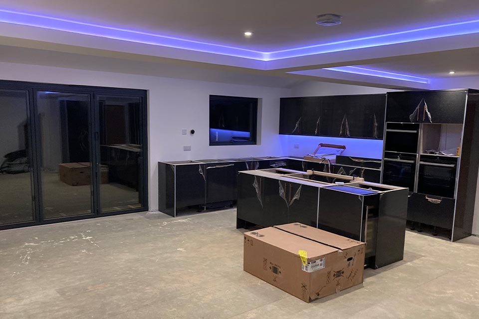 A kitchen in the process of being installed in a newly built rear extension with blue neon lighting.