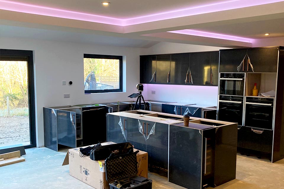 A kitchen in the process of being installed in a newly built rear extension with pink neon lighting.
