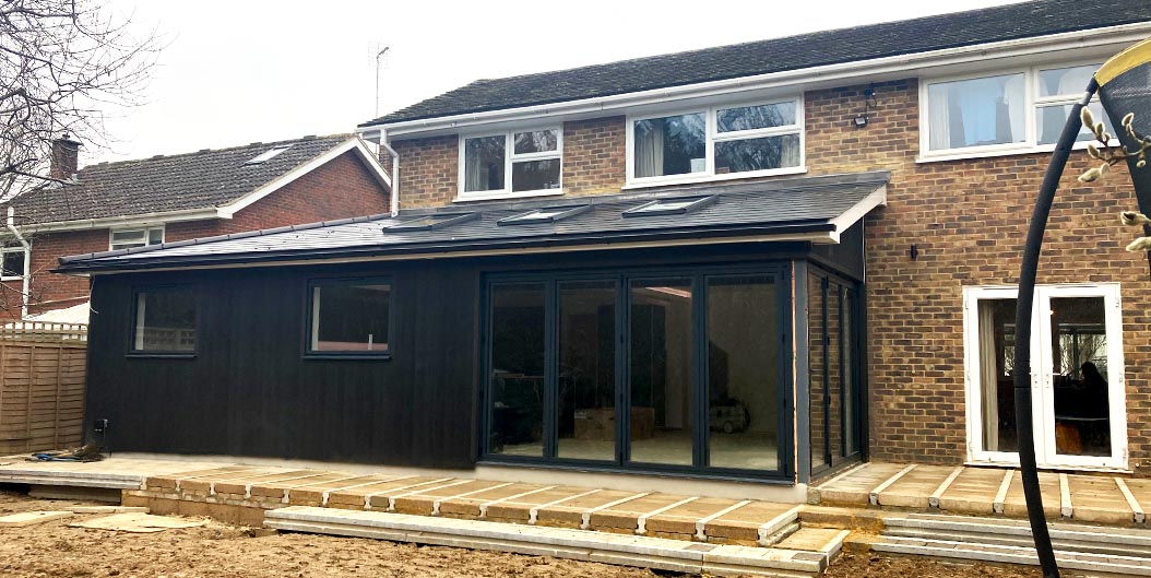 A newly built rear ground floor extension with a sloping roof, black cladding and large folding doors.