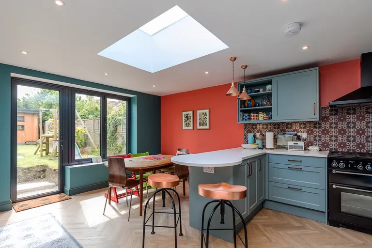 A rear kitchen extension with skylight window, wooden floor, copper top bar stalls, dining table and a striking orange feature wall.