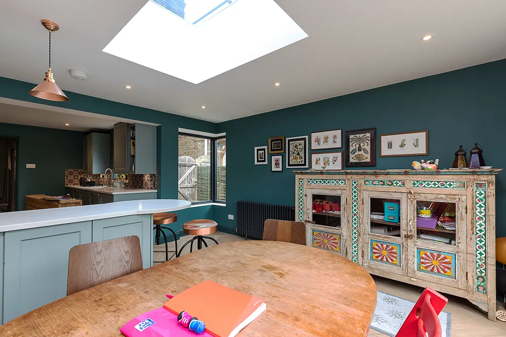 Kitchen extension with turquoise walls, dining table and a decorated wooden sibeboard.