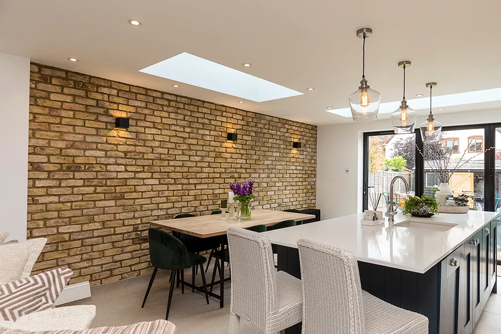 Kitchen and living room extension with a feature brick wall, kitchen island, large sky light and dining table.