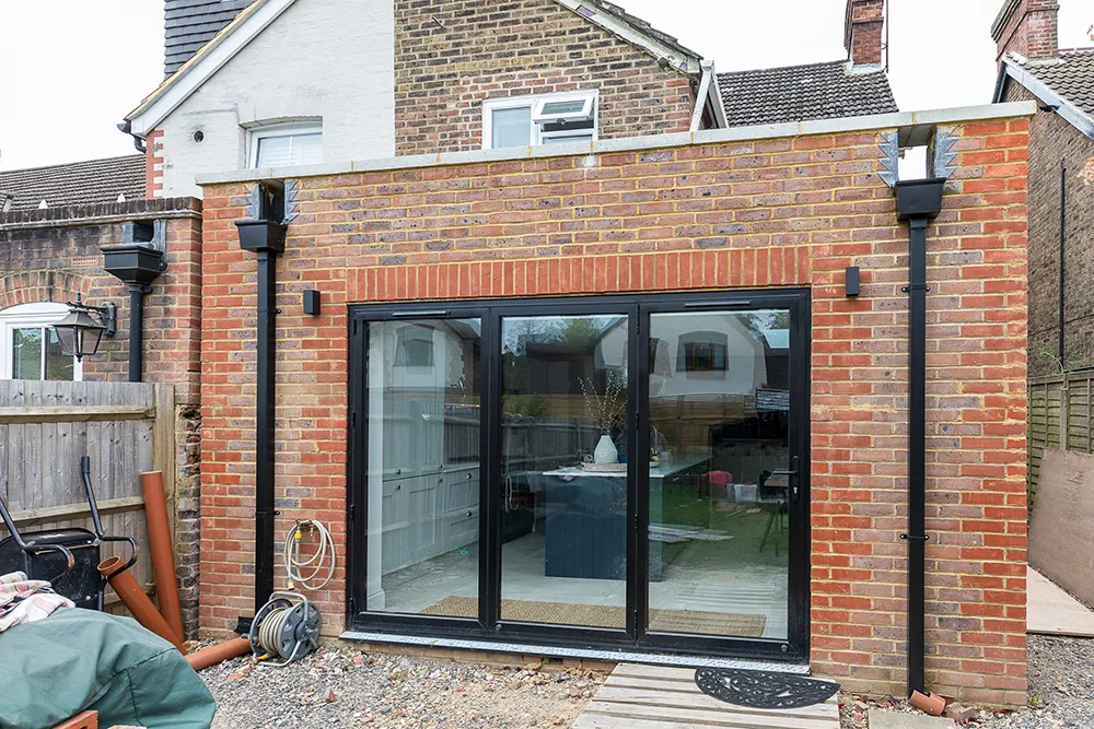 Exterior view of single storey rear extension with black patio frames and drainpipes.