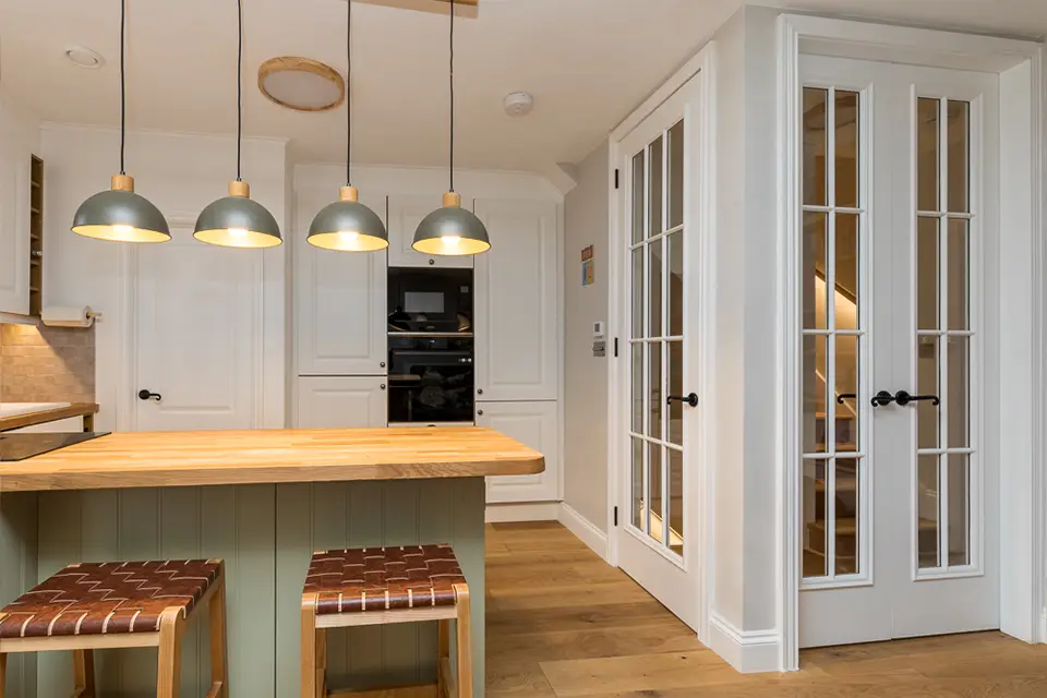 A kitchen with a breakfast bar, wooden worktop and white cupboards.